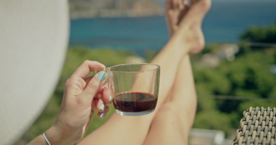 woman holding a drink with legs propped up overlooking body of water